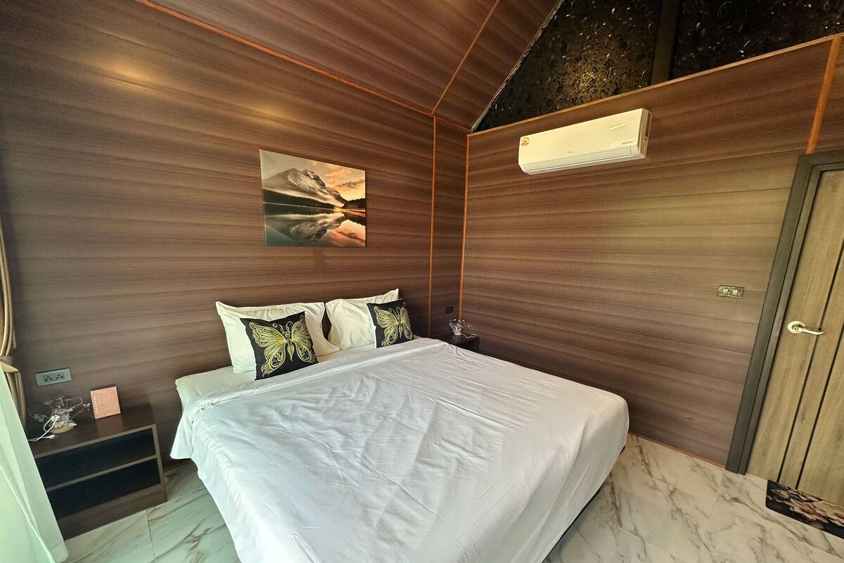 Un dormitorio moderno con una cama grande, paredes de madera, suelo de mármol y un cuadro de un paisaje montañoso.