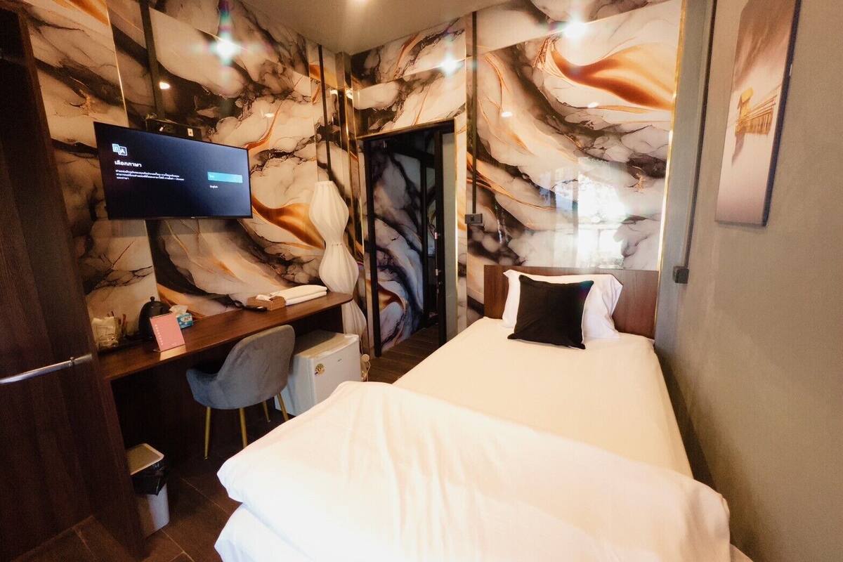 Habitación de hotel con cama, escritorio con silla, televisor y pared con diseño de mármol.