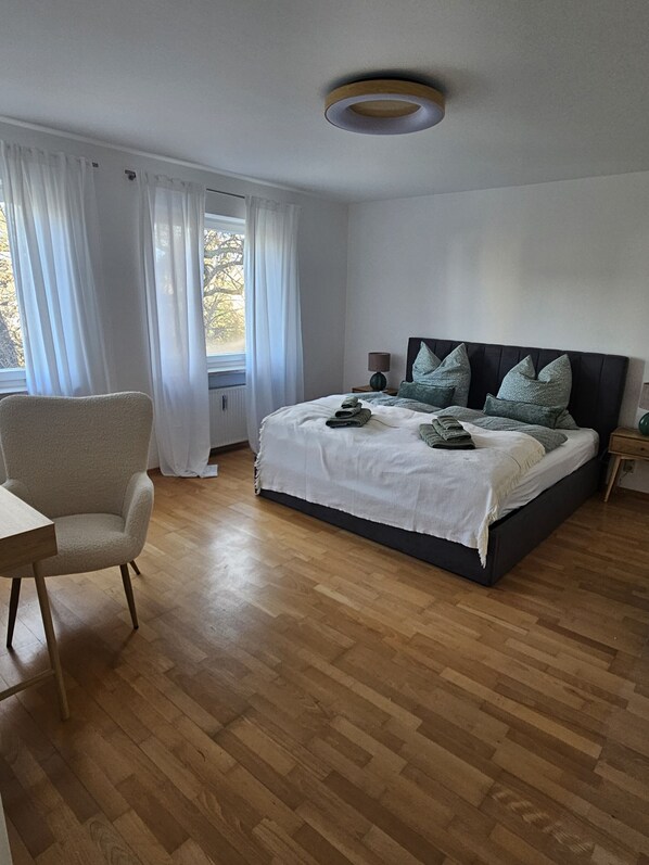 A bedroom with a bed, a chair, a nightstand, and a window with curtains.