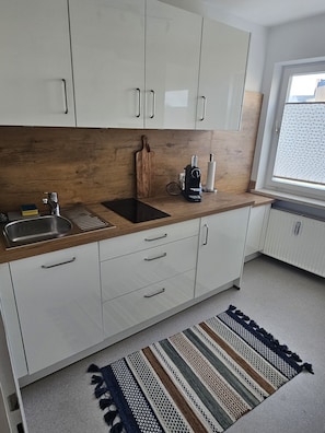 A modern kitchen with white cabinets, a wooden countertop, a sink, and a window with blinds.