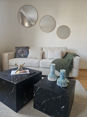 A living room with a striped sofa, two black marble coffee tables, and three round mirrors on the wall.