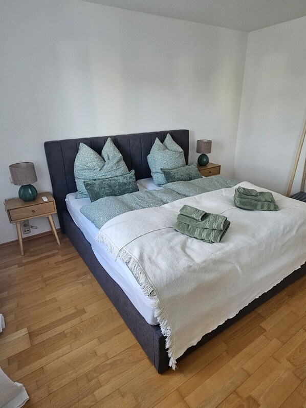 A neatly made bed with a white duvet and green pillows, a wooden nightstand with a lamp, and a wooden floor. - Premium apartment on Mühlbach in the center (Bad Aibling)