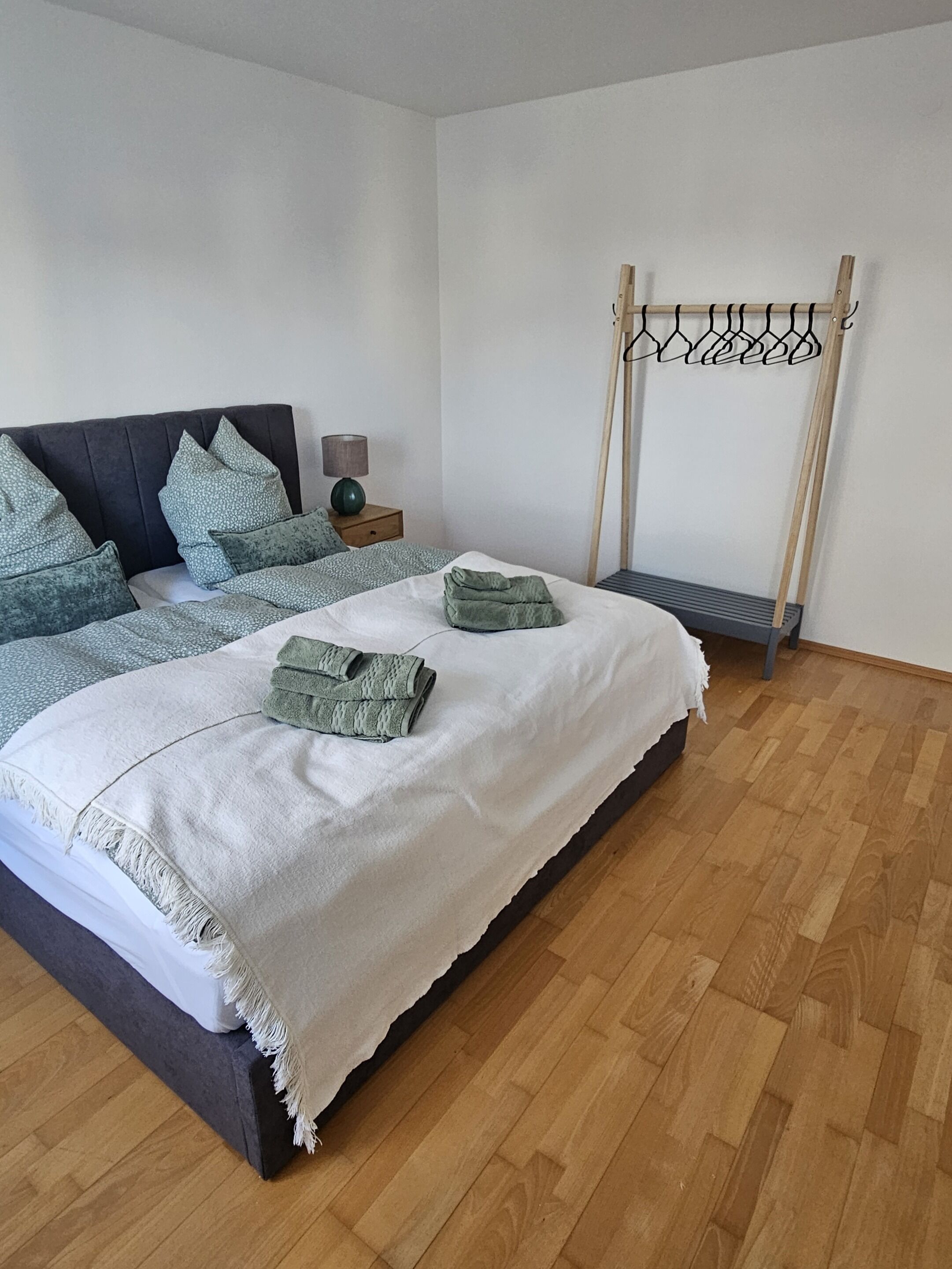 Ein Schlafzimmer mit einem Bett, Kissen, einem Nachttisch, einer Lampe und Holzdielen.