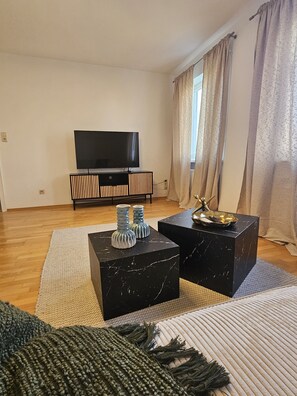 A modern living room with a flat-screen TV, black marble coffee tables, and a woven rug.