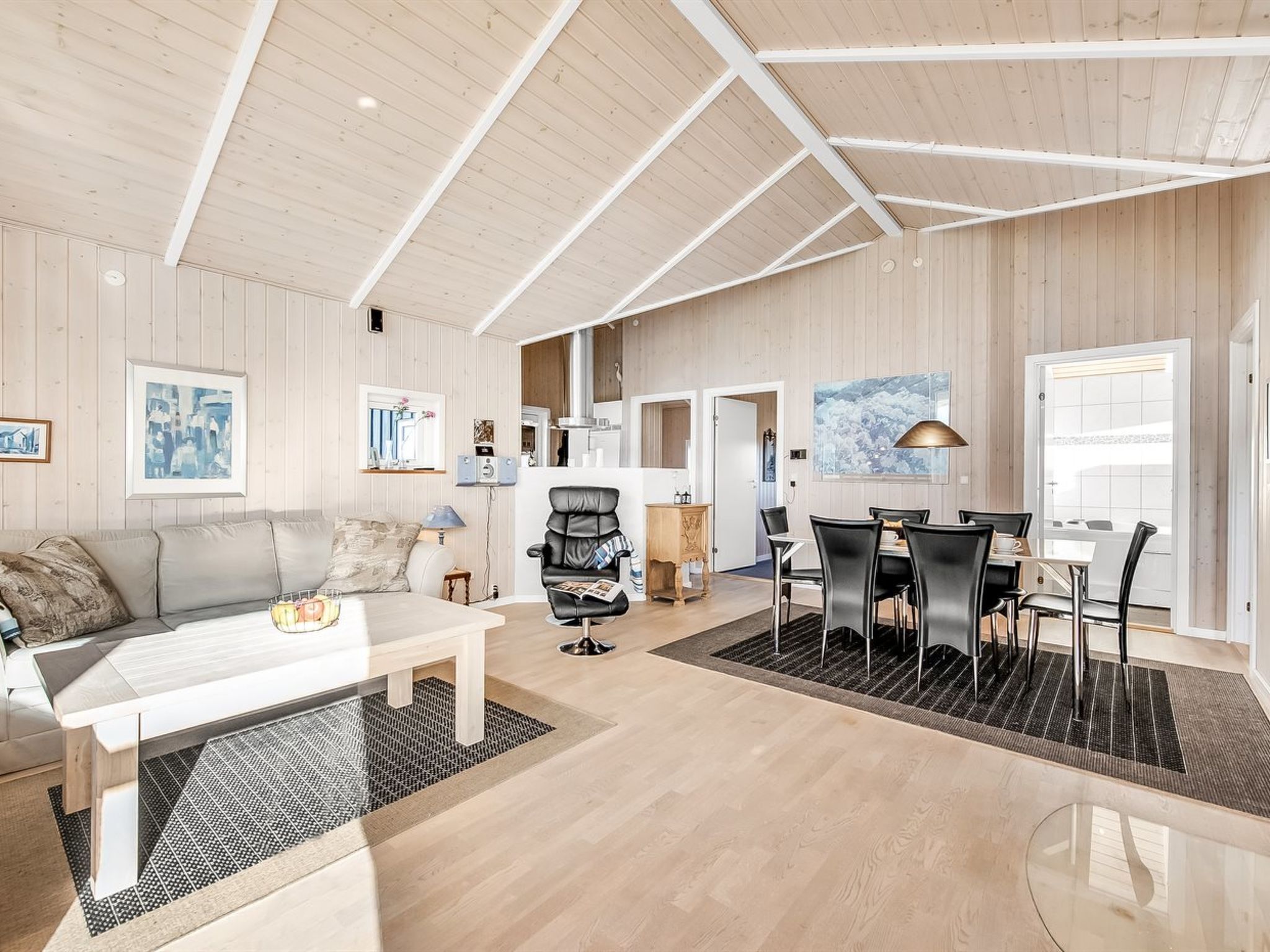A spacious living area with a sofa, coffee table, and dining table with chairs. There is a black leather chair and a rug on the floor.