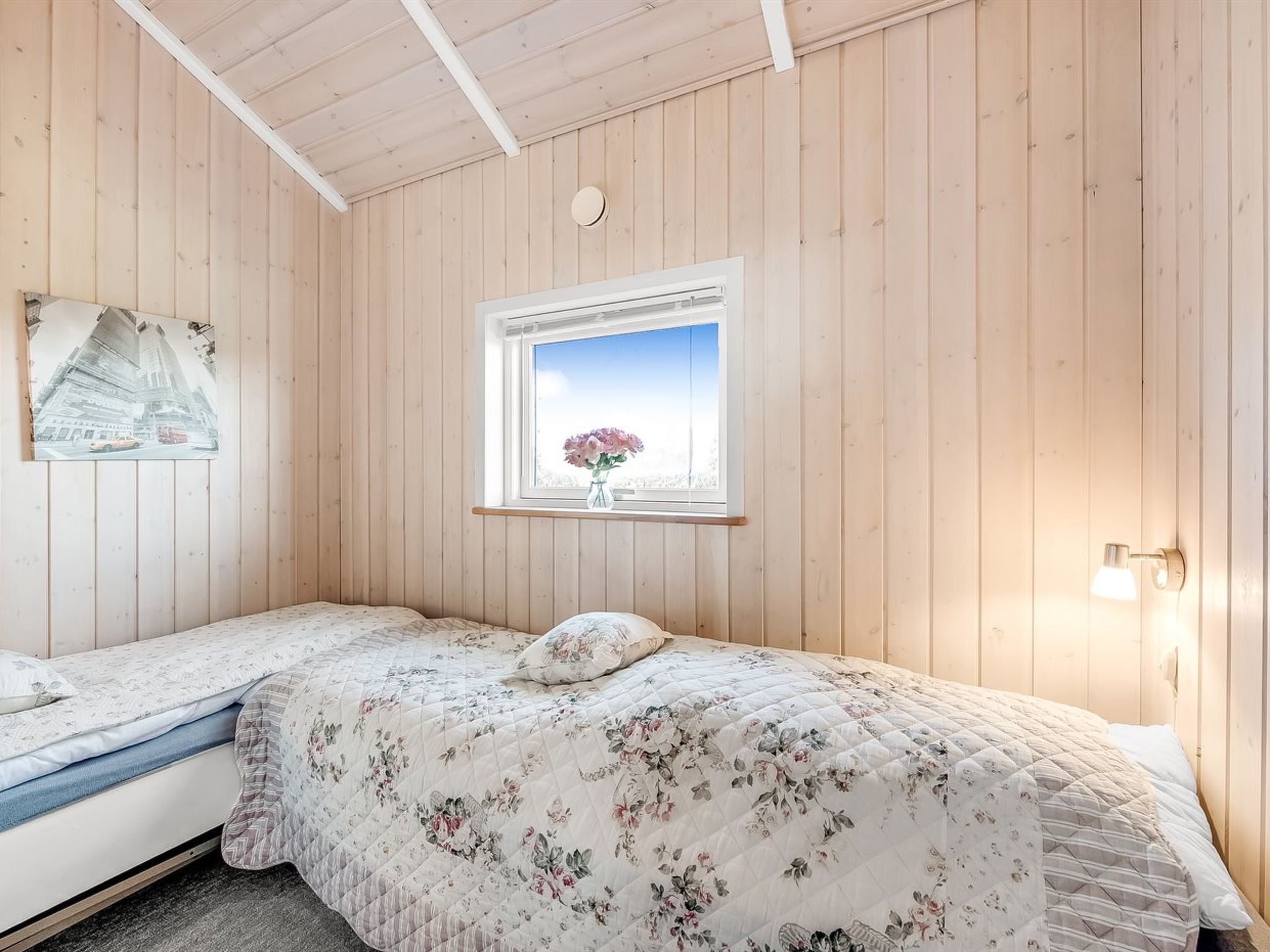 Een slaapkamer met twee bedden, een raam met uitzicht, een wandklok en een wandlamp.