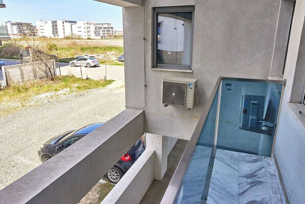 Un balcon avec une voiture garée en contrebas, une fenêtre et un immeuble en arrière-plan.