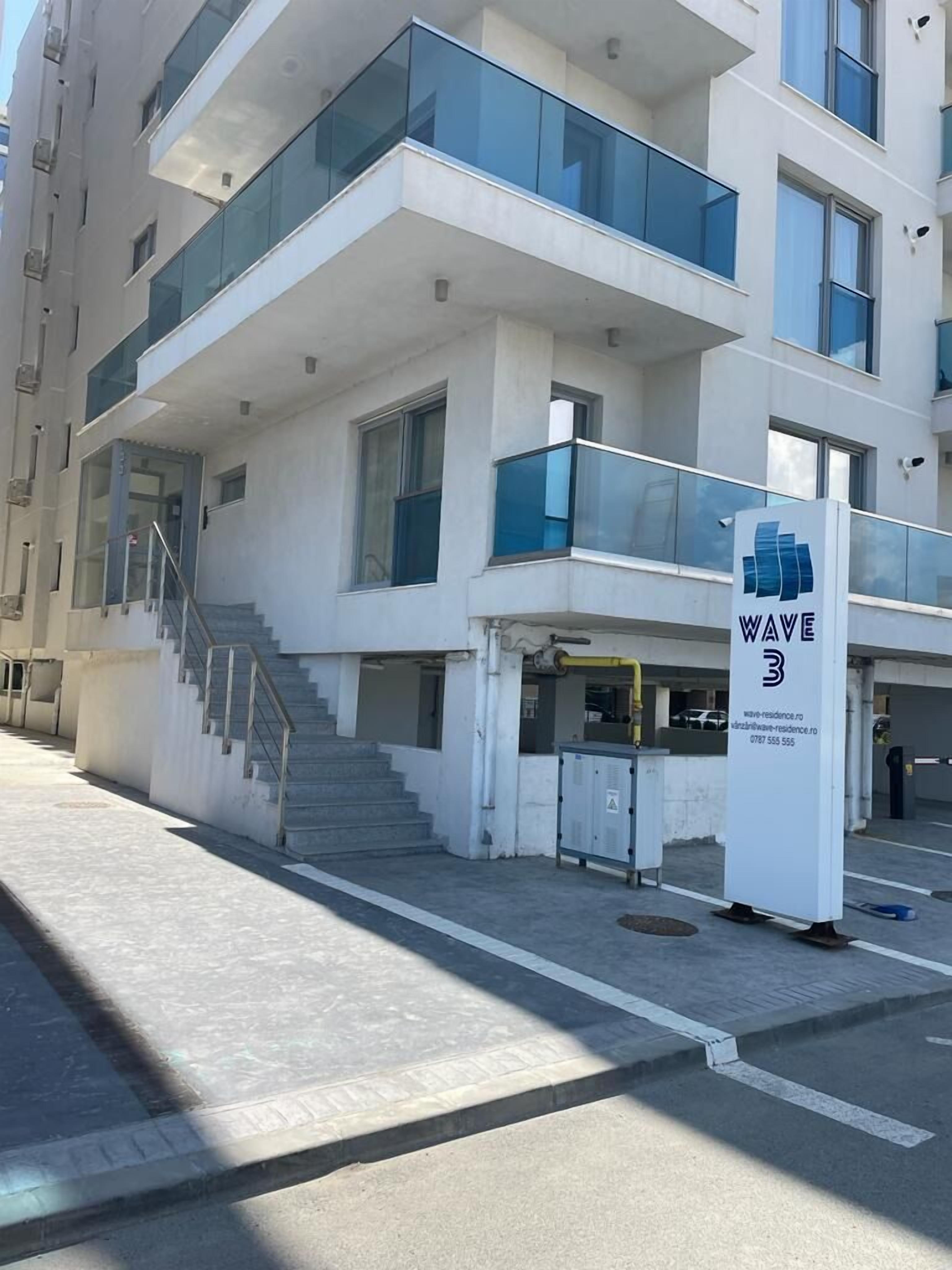 A modern multi-story building with a prominent sign for 'Wave 3' indicating a residential area.
