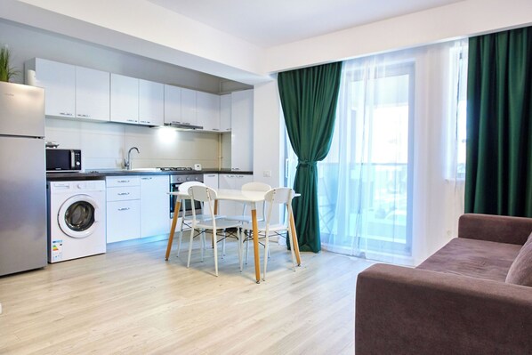 A modern kitchen with white cabinets, a washing machine, and a dining area with a table and chairs.