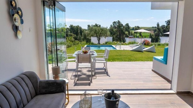 Ein modernes Wohnzimmer mit einer Couch, einem Esstisch und Blick auf eine Terrassenanlage mit Pool und Sitzgelegenheit.