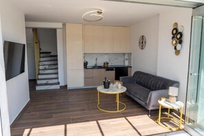 A modern living room with a grey sofa, a small round table, and a glass door leading to a balcony.