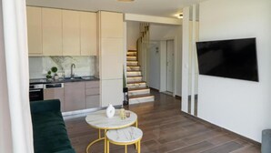Ein modernes Wohnzimmer mit einer Couch, einem kleinen runden Tisch, einer Treppe und einem an der Wand befestigten Fernseher.