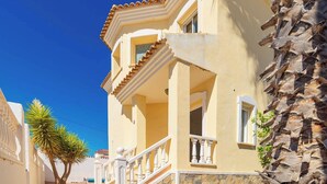 A two-story building with a balcony, a stone wall, and a palm tree. - Stunning Villa Rosa Quesada Centre private pool (Ciudad Quesada)