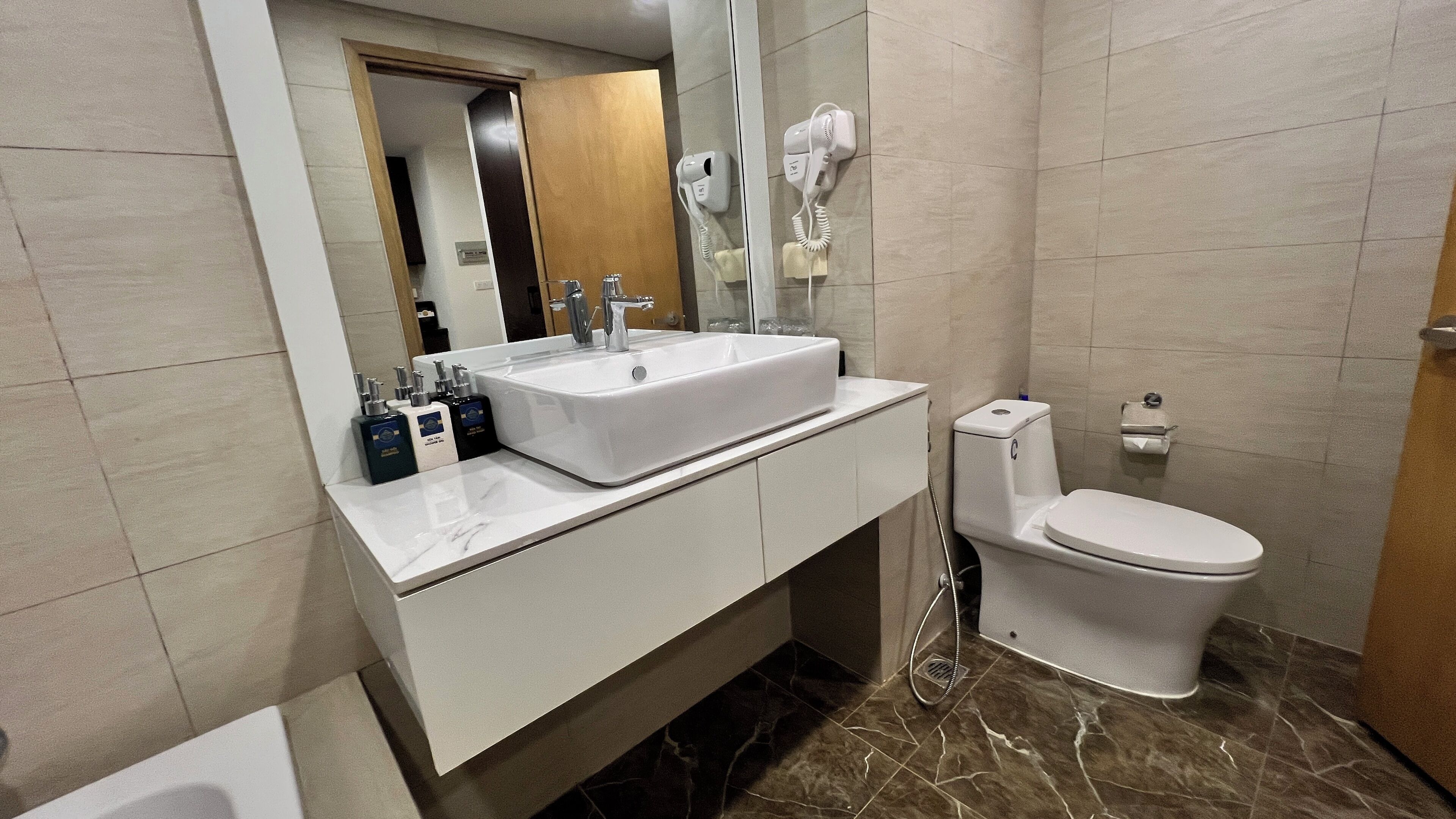 A modern bathroom with a white sink, mirror, and toilet. There are three toiletries on the sink counter.
