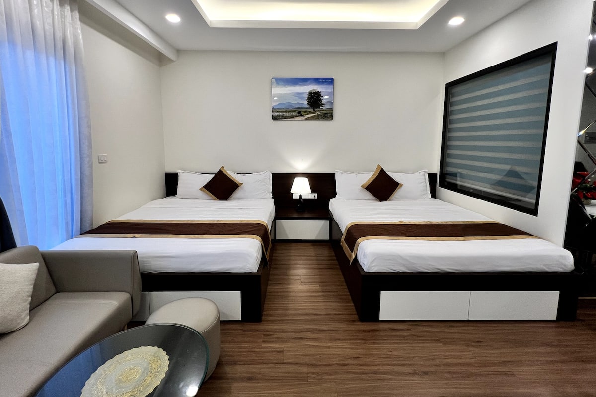 Habitación de hotel con dos camas, un sofá, un escritorio y un ventanal grande.