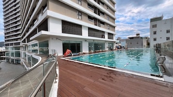 Uma piscina no terraço com deck de madeira, cercada por edifícios modernos com varandas.
