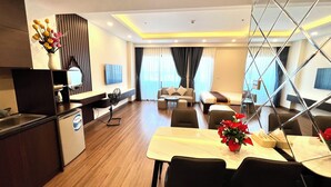 A modern hotel room with a dining area, a sofa, a bed, and a TV. - Stunning Ocean View Apartment in FLC Sea Tower (Quy Nhon Nam)