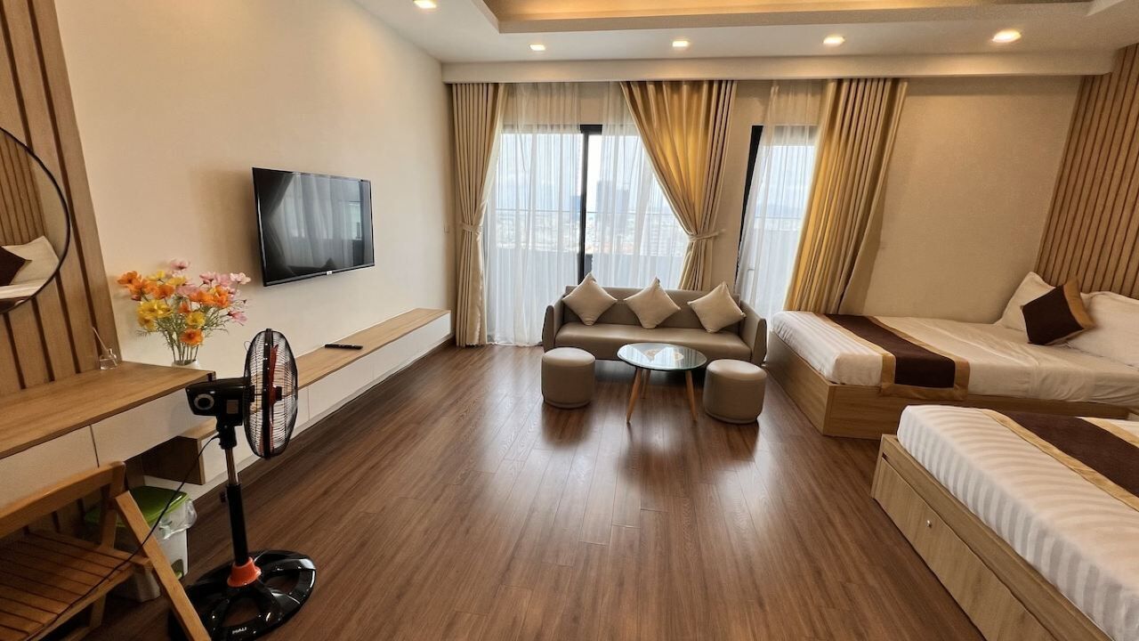 A modern hotel room with a sofa, a bed, a TV, and a wooden floor.