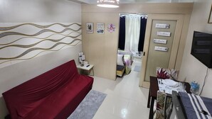 A modern hotel room with a red sofa, a small table with a lamp, a bed with a curtain, and a TV on a stand. - MNM Place - Sea Residence - 0A (Pasay)