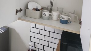 A kitchen with white cabinets, a white countertop, and a black backsplash. There are three mugs on the counter, one with a blue handle. - MNM Place - Sea Residence - 0A (Pasay)