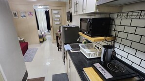 A compact kitchen with a microwave, stove, and sink. There is a small dining area with a table and chairs. - MNM Place - Sea Residence - 0A (Pasay)