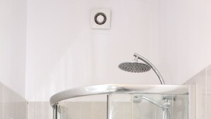 A glass-enclosed shower stall with a handheld showerhead, a towel rack, and a small vent on the wall.