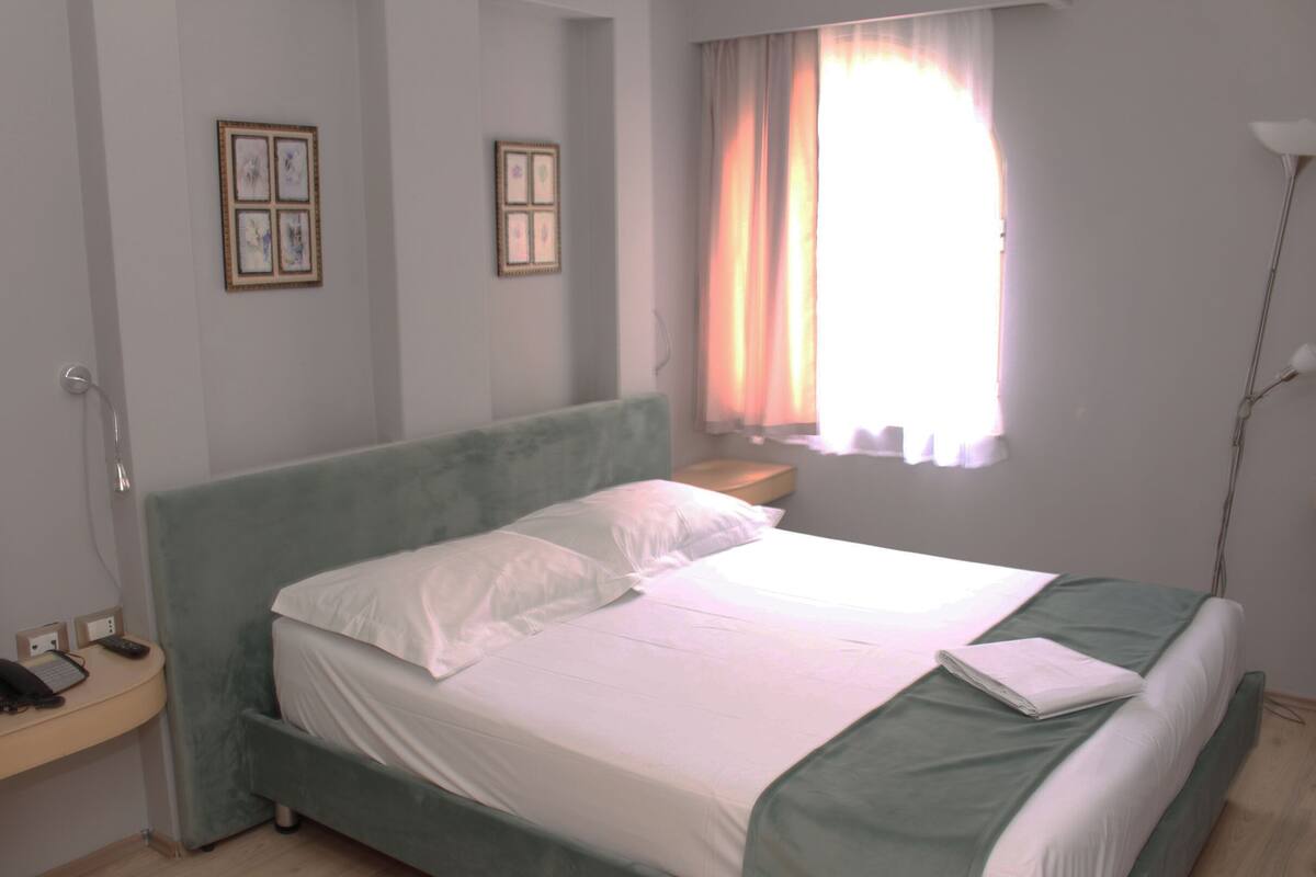 A neatly made bed with white linens and a green headboard in a hotel room.