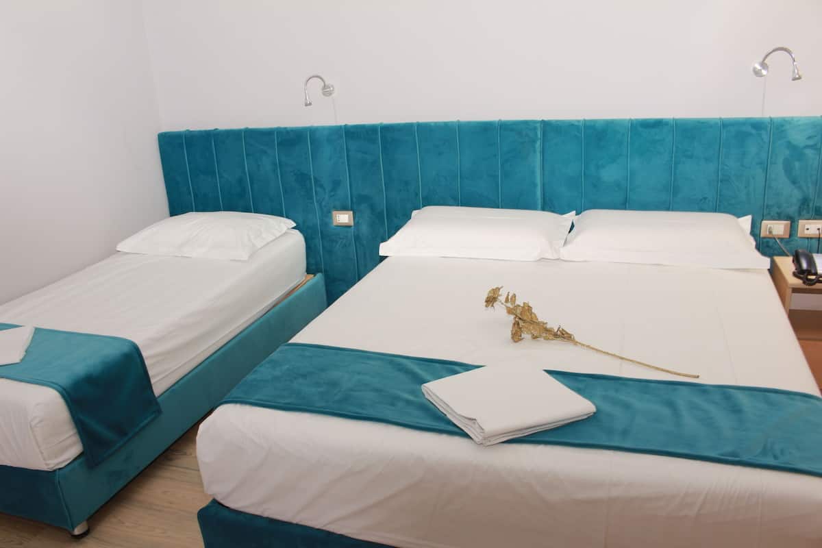 A hotel room with two single beds, each with teal headboards and white bedding.