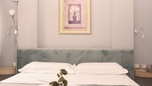 A neatly made bed with white linens, a framed artwork above it, and a bedside lamp on the left.
