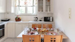 A kitchen with white cabinets, a dining table set with plates, glasses, and a fruit basket. - Casa Valore by 8essentially (Chania)