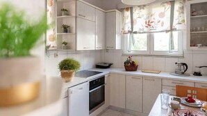 A modern kitchen with white cabinets, a stove, and a window with floral curtains. - Casa Valore by 8essentially (Chania)