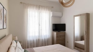 A bedroom with a bed, a television on a wooden dresser, a large mirror, and a window with sheer curtains. - Casa Valore by 8essentially (Chania)
