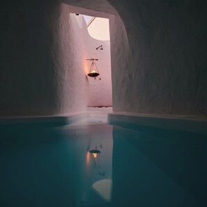 Una piscina interior con vista despejada al techo y a las paredes, un colgante de luz y una superficie de agua tranquila.