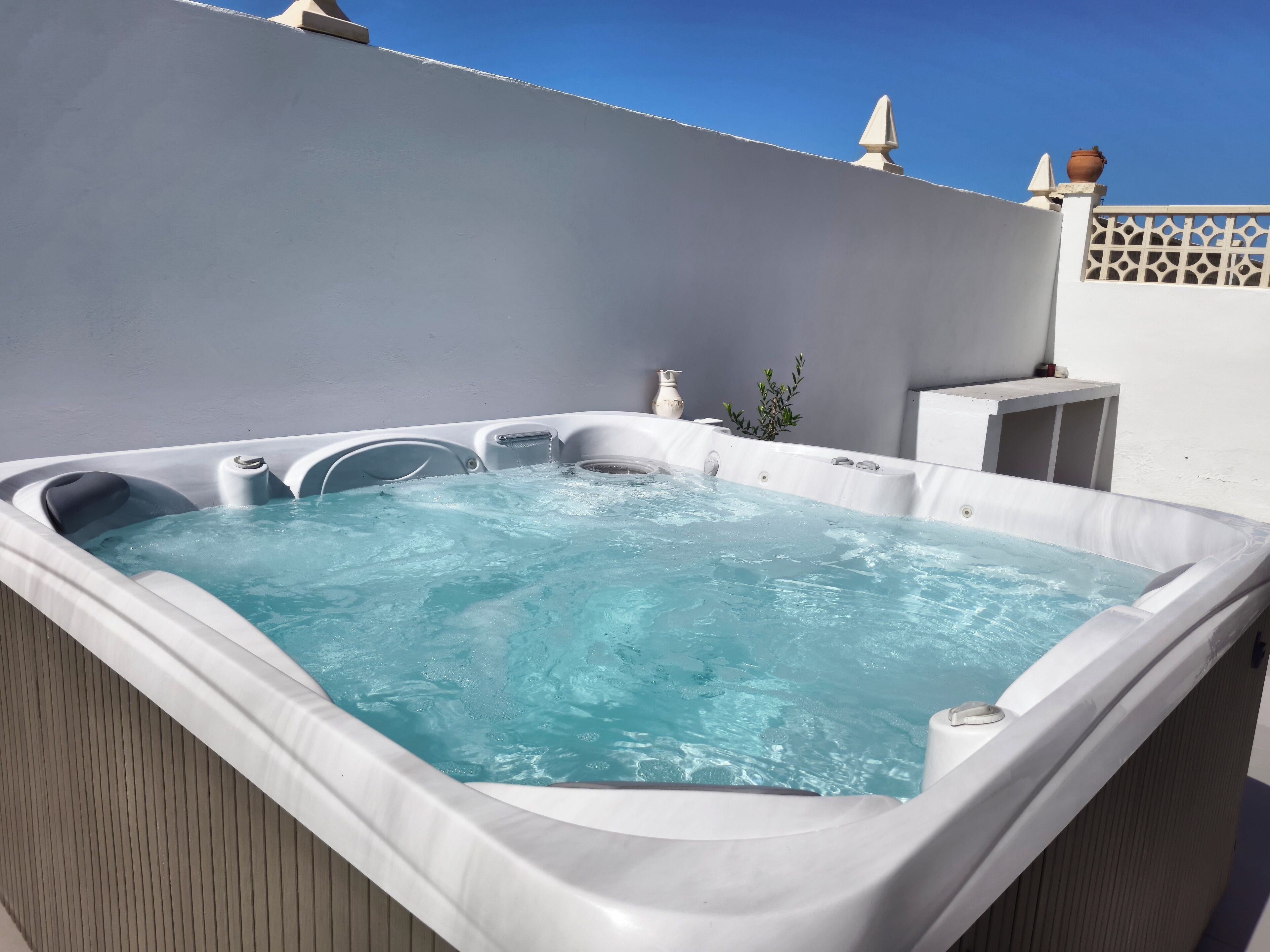 Un bain à remous avec une fontaine à eau d’un bleu cristallin, entouré d’un mur blanc et d’une terrasse en bois.