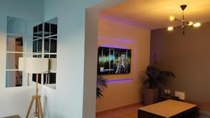 En moderne stue med et stort fladskærms-tv monteret på væggen, en gulvlampe, et sofabord og en loftlampe.