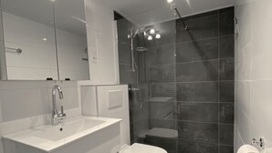 Une salle de bain moderne avec un meuble-lavabo blanc, des toilettes, une douche dotée d’une paroi en verre et un grand miroir.