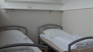 Une chambre de dortoir avec deux lits superposés en métal, des murs blancs, un plafond en bois et une petite étagère au-dessus des lits.