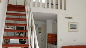 Una scala conduce a una camera soppalcata con una cucina sullo sfondo.