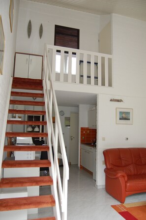 A staircase leading to a loft bedroom with a kitchen in the background. - Family-friendly vacation home, attractively furnished, directly on the waterfront (Bruinisse)