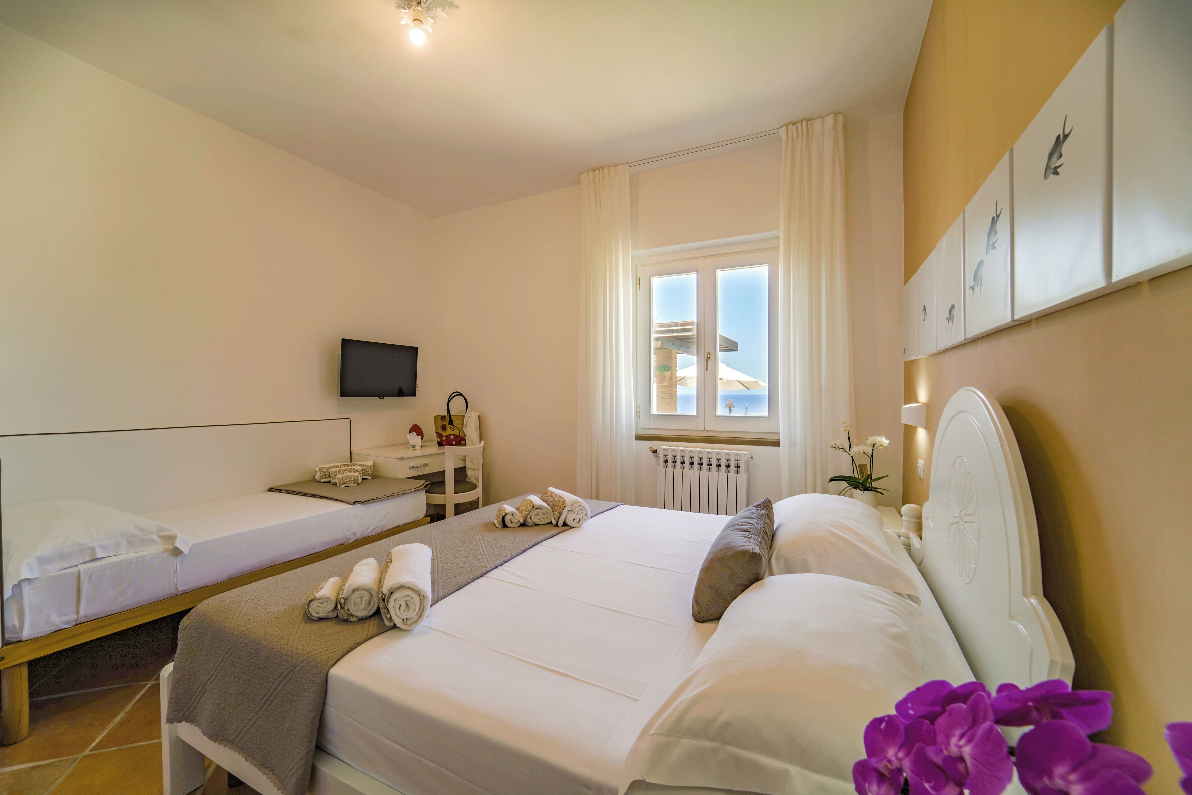 A hotel room with two beds, a TV, a small table with a lamp, and a window with curtains.
