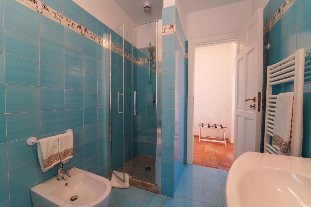 Ein Badezimmer mit blauen Fliesen, einer Duschkabine aus Glas, einem Waschbecken und einer weißen Badewanne.