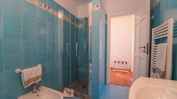 Ein Badezimmer mit blauen Fliesen, einer Duschkabine aus Glas, einem Waschbecken und einer weißen Badewanne.