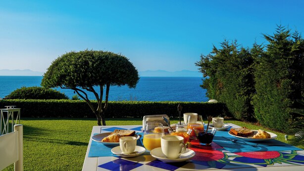 A table set for breakfast with a view of the sea, including plates of food, cups, and a glass of juice. - Le casette di Ulisse (Castellabate)