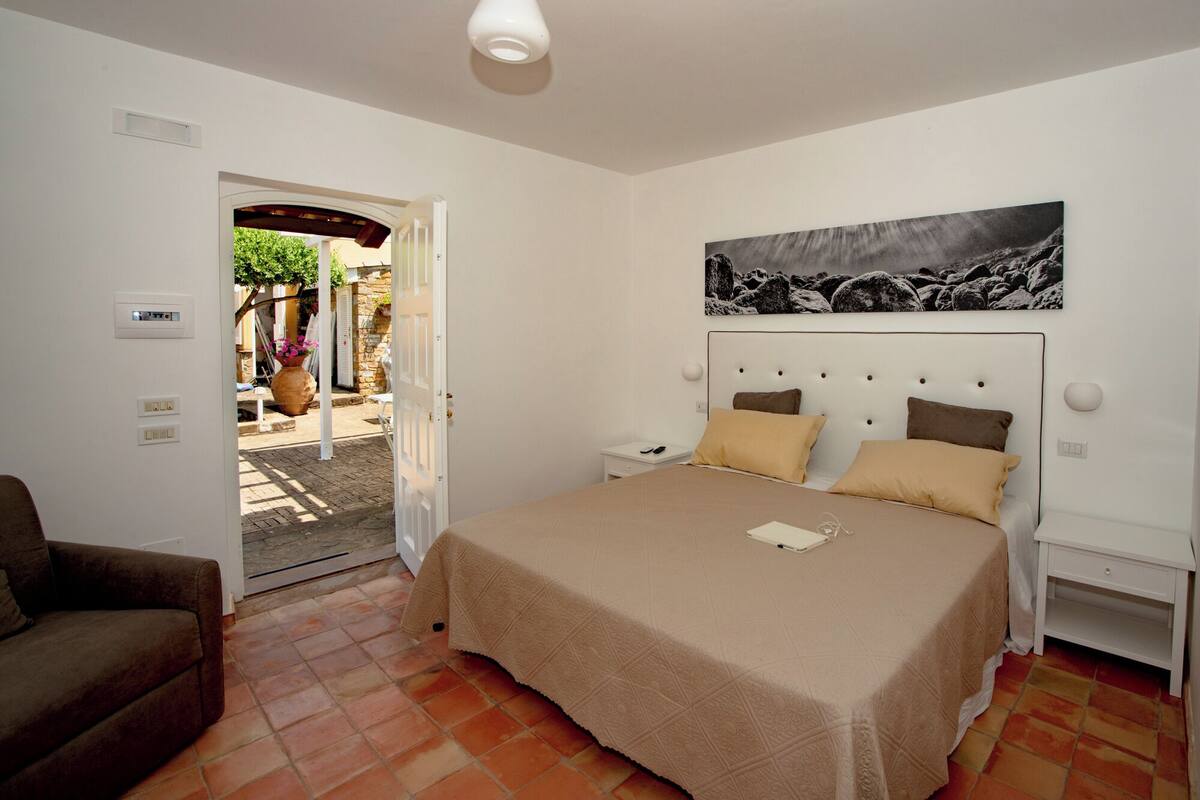 Een slaapkamer met een bed, nachtkastjes, een deur naar een buitenruimte en een kunstwerk aan de muur.
