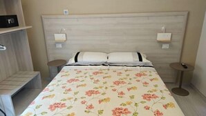 Une chambre d’hôtel comprenant un lit, deux tables de chevet, une petite table et une étagère.