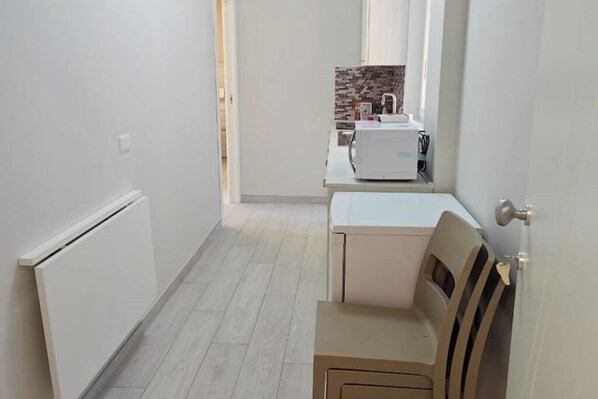 A narrow hallway with a radiator, a white door, and a small table with a chair. - GS Apartments Tropea - Gold (Tropea)