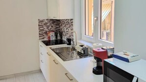 Une petite cuisine avec des meubles blancs, un plan de travail carrelé, un évier et une fenêtre donnant sur un balcon.