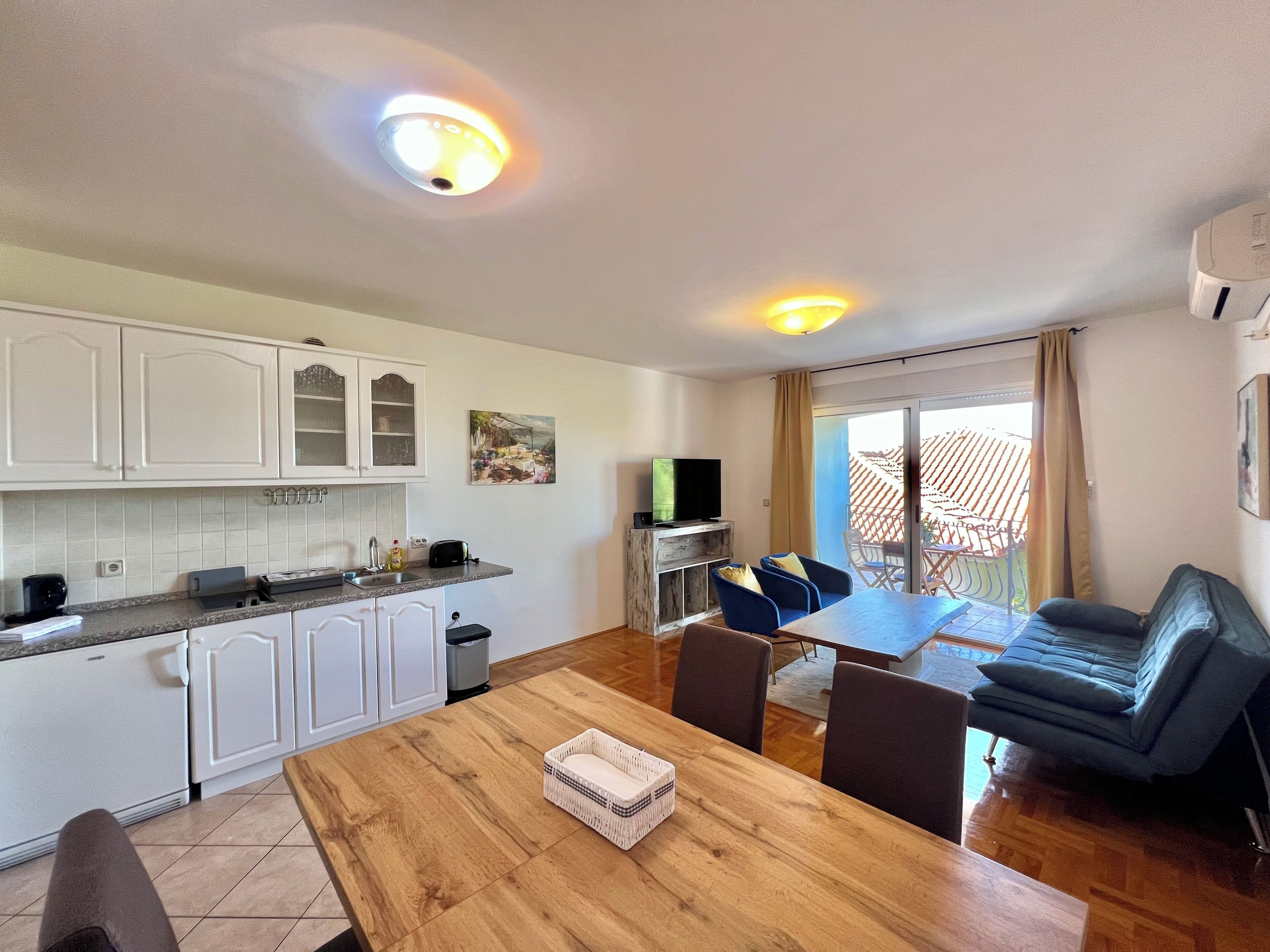 A modern kitchen with white cabinets, a dining area with a wooden table, and a balcony with a view.