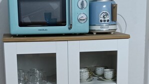 A white cabinet with glass doors, containing kitchenware and a microwave on top.