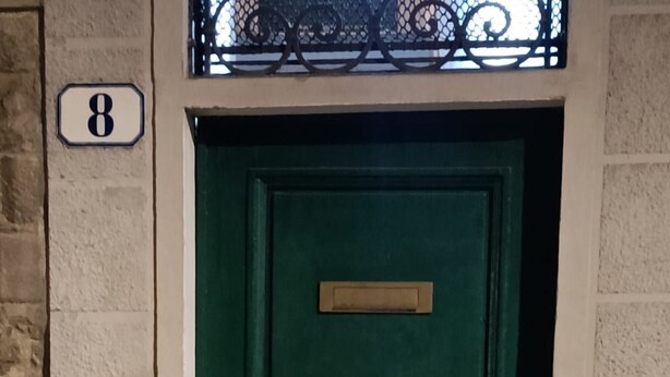 A green door with a brass plate, a keypad, and a number '8' sign on the wall.